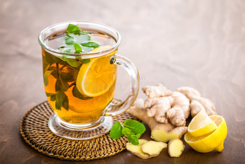 Hot herbal tea with fresh lemon, ginger and mint leaves on brown background