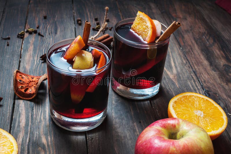 Hot mulled wine with spices, apple and orange on wood background