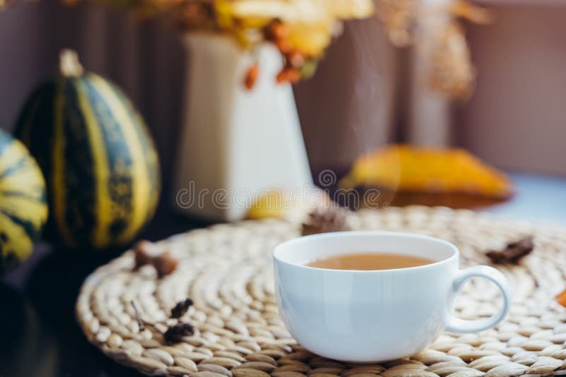 Hot steaming cup of coffee, tea with autumn bouquet, falling leaves, decorative pumpkin, cones on straw napkin. Natural decoration stock photos Hot steaming cup of coffee, tea with autumn bouquet, falling leaves, decorative pumpkin, cones on straw napkin. Natural decoration stock photos