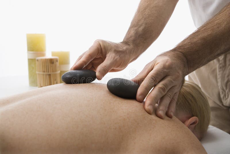 Caucasian middle-aged male massage therapist placing hot stones on back of Caucasian middle-aged woman lying on massage table. Caucasian middle-aged male massage therapist placing hot stones on back of Caucasian middle-aged woman lying on massage table.