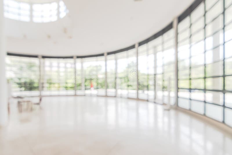 Hotel or office building lobby blur background interior view toward reception hall, modern luxury white room space with blurry corridor and building glass wall window.