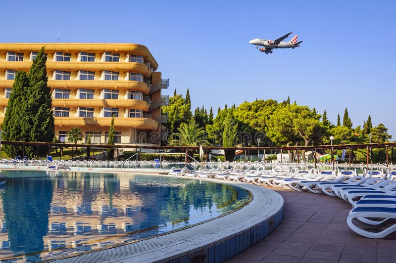 A hotel for tourists, a swimming pool with sun beds and an airplane flying over them in the early summer morning. Croatia, Europe