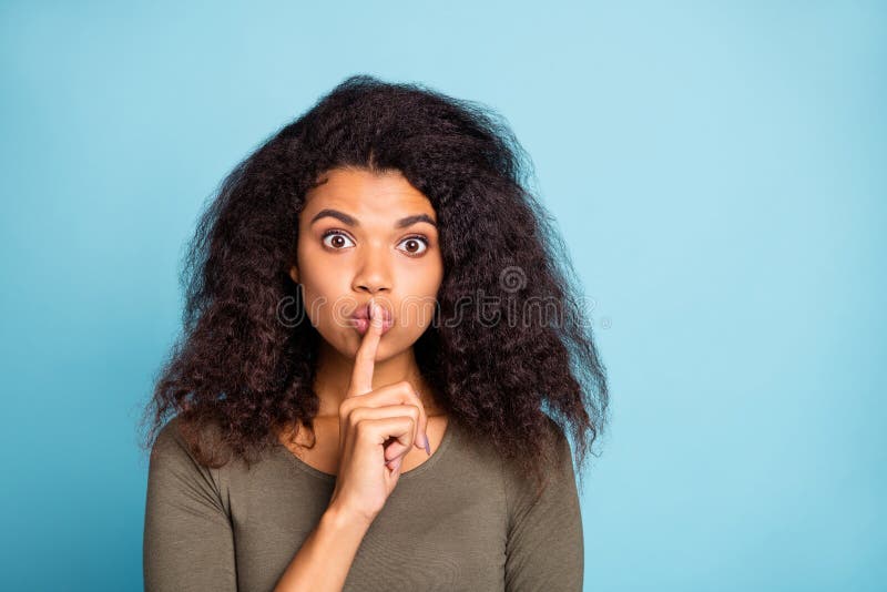 Keep secret. Close up photo of serious afro american girl hold her index finger, near lips show mute sign tell dont share private novelty wear stylish green pullover isolated blue color background. Keep secret. Close up photo of serious afro american girl hold her index finger, near lips show mute sign tell dont share private novelty wear stylish green pullover isolated blue color background