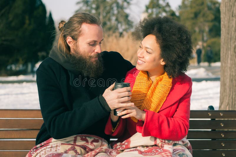 Loving couple with hot drinks sitting on bench in winter. Christmas time. Loving couple with hot drinks sitting on bench in winter. Christmas time
