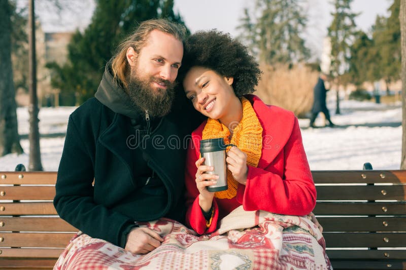Loving couple with hot drinks sitting on bench in winter. Christmas time. Loving couple with hot drinks sitting on bench in winter. Christmas time