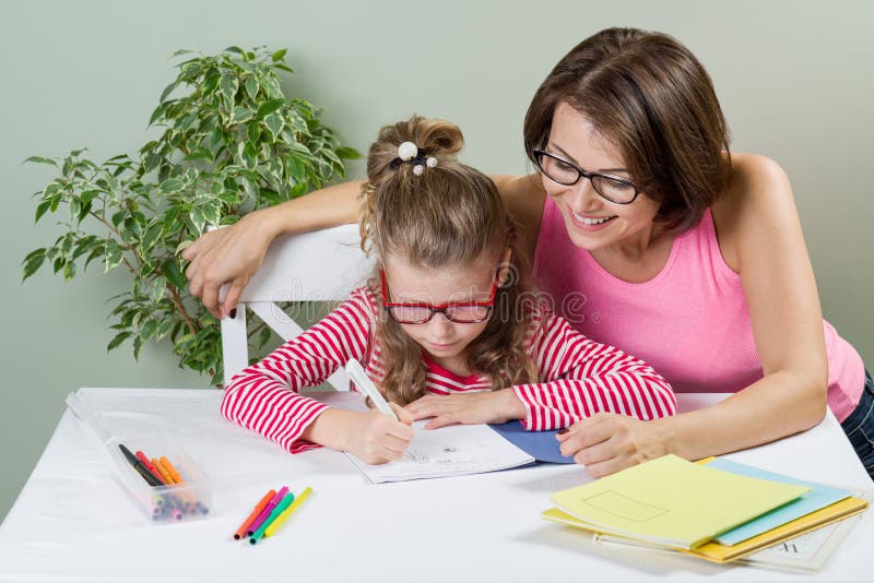 Houdende van moeder die haar dochter elementaire scholier helpen in haar notitieboekje, thuis bij de lijst schrijven stock foto's Houdende van moeder die haar dochter elementaire scholier helpen in haar notitieboekje, thuis bij de lijst schrijven stock foto's