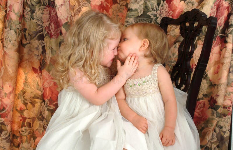 Loving sisters sitting together on antique chair, on floral background. Loving sisters sitting together on antique chair, on floral background