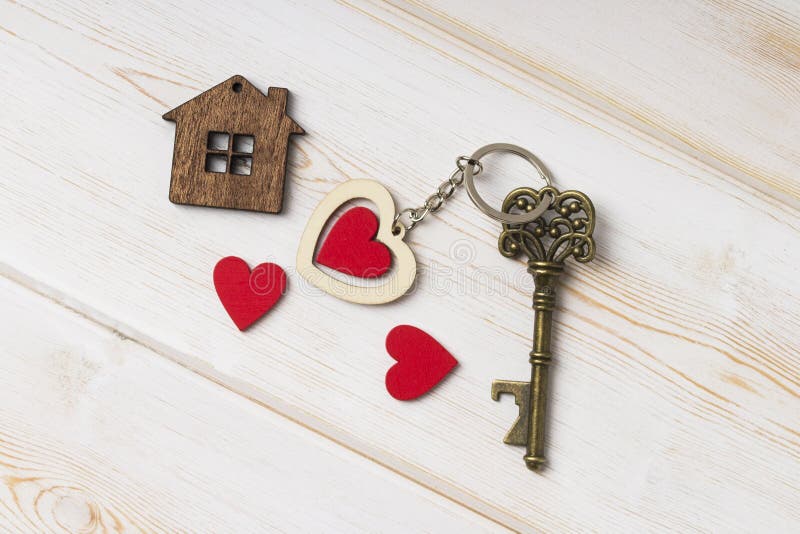 House key with home keyring decorated with wooden  heart.  Old key with a heart on white wood . sweet home concept