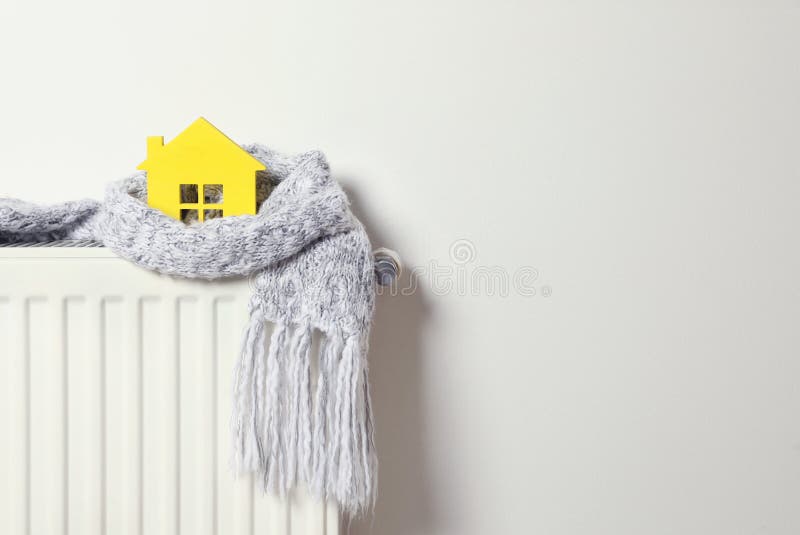 House model wrapped in scarf on radiator, space for text. Winter heating efficiency