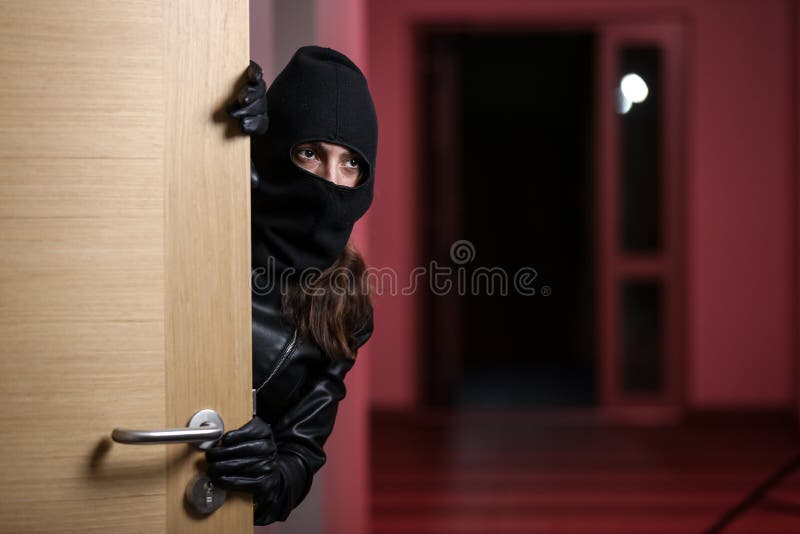 House robbery by woman in a black jacket and black mask holding black gun. Burglar in a mask. Thief in a mask. Trying to break into other people`s apartments