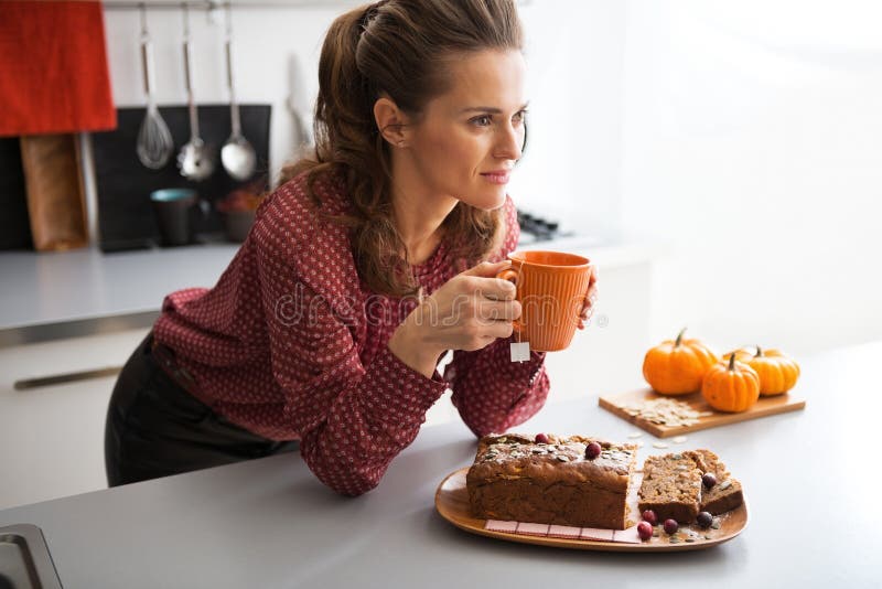 Happy young housewife drinking tea with freshly baked pumpkin bread with seeds in kitchen. Happy young housewife drinking tea with freshly baked pumpkin bread with seeds in kitchen