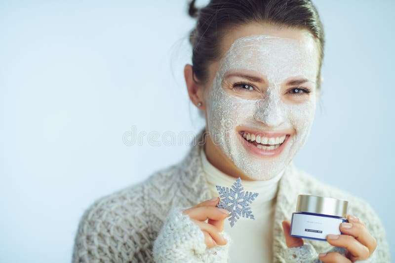 Housewife with facial mask holding snowflake and cosmetic jar