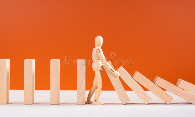 Wooden man stopping falling domino concept. Symbol of crisis, risk, management, leadership and determination. Domino effect. Fall of the crumbling business is saved by mannequin. Orange background. Wooden man stopping falling domino concept. Symbol of crisis, risk, management, leadership and determination. Domino effect. Fall of the crumbling business is saved by mannequin. Orange background.