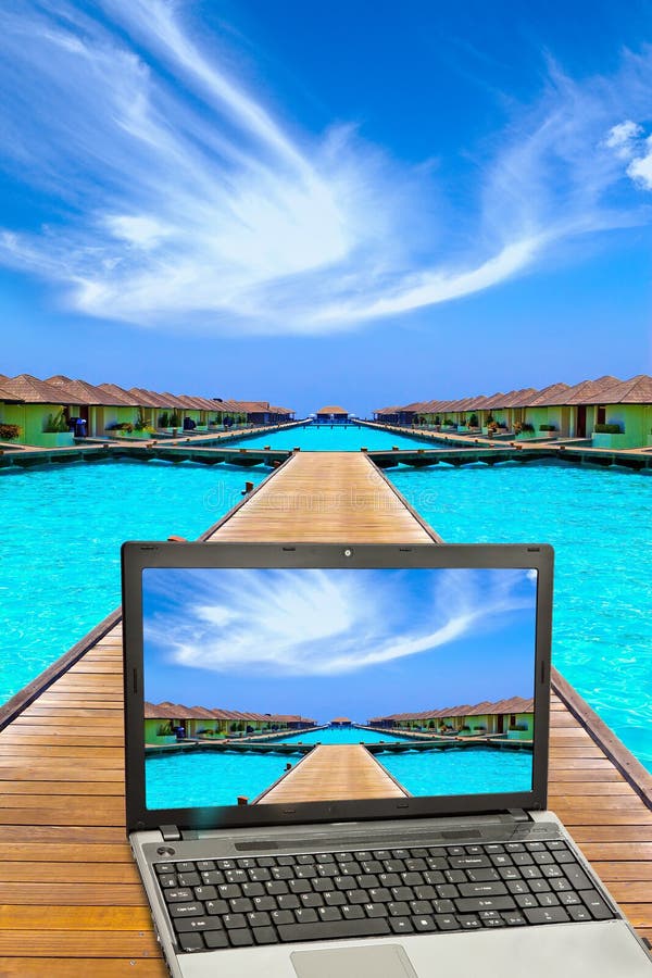 Wooden road to small houses over the sea and the laptop with a beach picture. Wooden road to small houses over the sea and the laptop with a beach picture