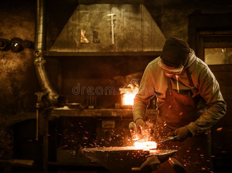 The blacksmith forging the molten metal on the anvil in smithy. The blacksmith forging the molten metal on the anvil in smithy.