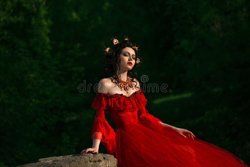 The lady in lush red dress with open shoulders. Around her neck is unusually luxurious decoration.The head decorated with a crown handmade.The fairy Princess was sitting on a rock, dreamy head thrown back.Fantastic shot. Fashionable toning. Creative computer colors. The lady in lush red dress with open shoulders. Around her neck is unusually luxurious decoration.The head decorated with a crown handmade.The fairy Princess was sitting on a rock, dreamy head thrown back.Fantastic shot. Fashionable toning. Creative computer colors.