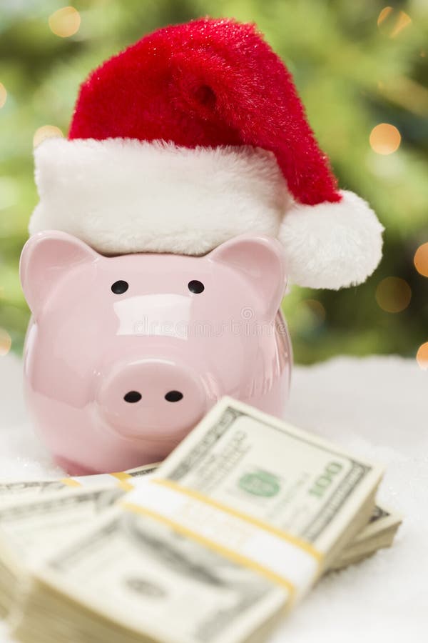 Hucha rosada que lleva a Santa Hat Near Stacks del dinero en Snowfl foto de archivo libre de regalías Hucha rosada que lleva a Santa Hat Near Stacks del dinero en Snowfl foto de archivo libre de regalías