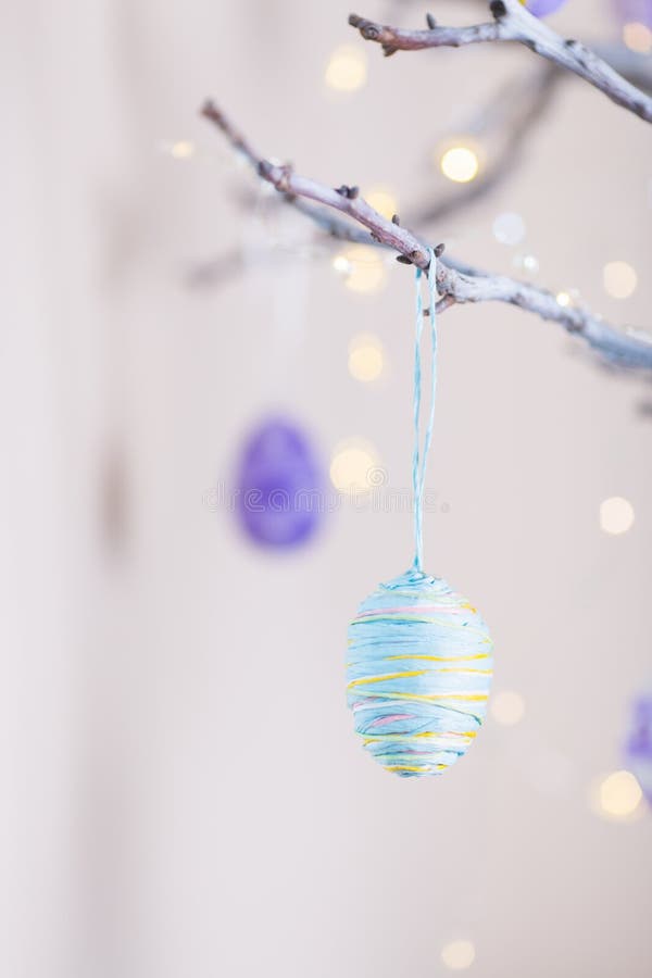 Huevo de Pascua colorido adornado que cuelga en la rama de árbol interior con el bokeh caliente en el fondo blanco fotos de archivo libres de regalías Huevo de Pascua colorido adornado que cuelga en la rama de árbol interior con el bokeh caliente en el fondo blanco fotos de archivo libres de regalías