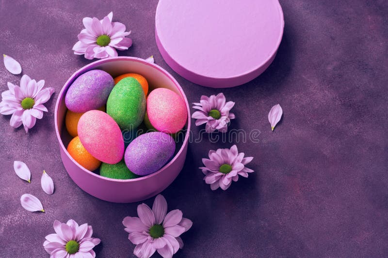 Huevos de Pascua brillantes coloridos en una caja de regalo redonda en el fondo púrpura adornado con las flores Visión de arriba, imagenes de archivo Huevos de Pascua brillantes coloridos en una caja de regalo redonda en el fondo púrpura adornado con las flores Visión de arriba, imagenes de archivo