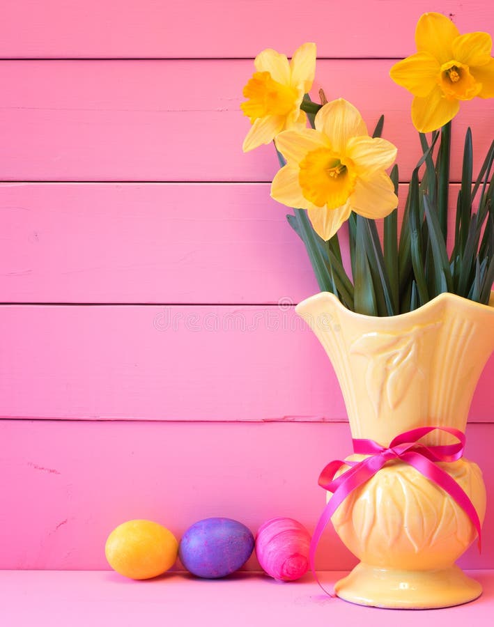 Huevos de Pascua coloridos en jerarquía con los narcisos en florero en fondo rosado de los tableros con el sitio o el espacio par fotos de archivo Huevos de Pascua coloridos en jerarquía con los narcisos en florero en fondo rosado de los tableros con el sitio o el espacio par fotos de archivo