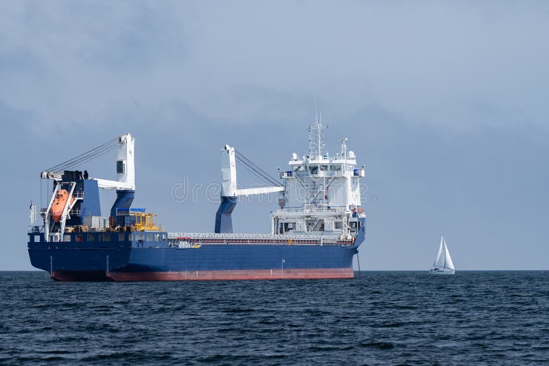 Huge Cargo Ship and Small Sailboat in the Open Sea. Concept of