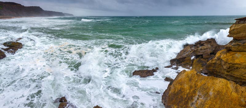A huge ocean waves breaking on the coastal cliffs in at the cloudy stormy day. Breathtaking romantic panoramic seascape of ocean