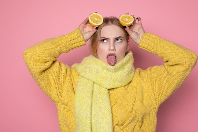 Human emotions. Blonde beautiful european girl in yellow sweater and scarf showing funny face, holding two sliced citrus royalty free stock photos Human emotions. Blonde beautiful european girl in yellow sweater and scarf showing funny face, holding two sliced citrus royalty free stock photos