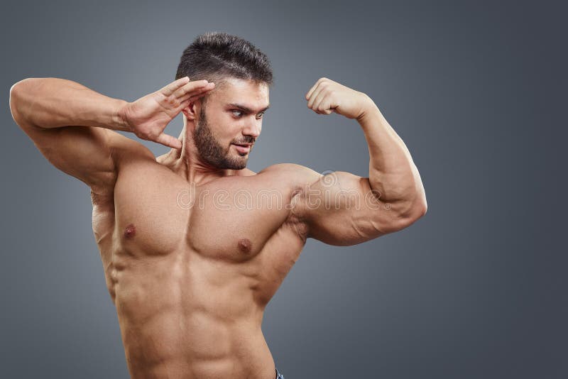 Human Muscle Bicep Growth concept. Strong man surprised of his muscular arm isolated on grey background.