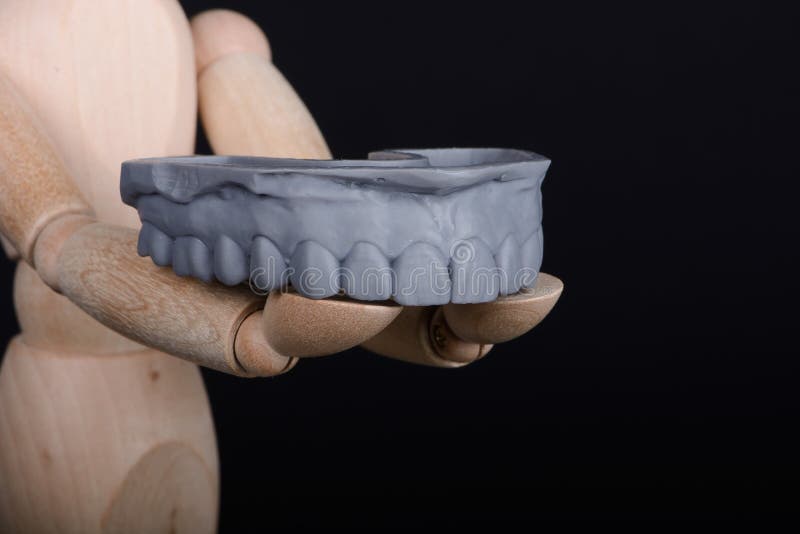 Human wooden figure holds in hands a dental upper jaw model printed on 3d printer on a black background.