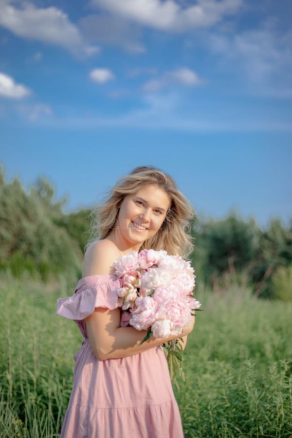 Humeur romantique. belle blonde avec cheveux lâche dans les stands avec bouquet de pivoines roses dans la nature. images stock