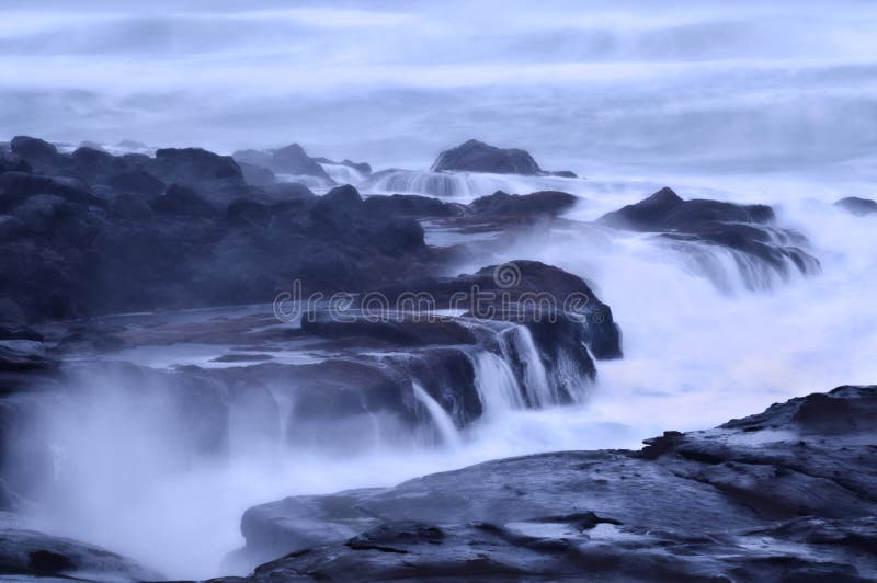 Moody ocean seascape with landscape of rocky beach with cool blue tint of soft waves. Moody ocean seascape with landscape of rocky beach with cool blue tint of soft waves.