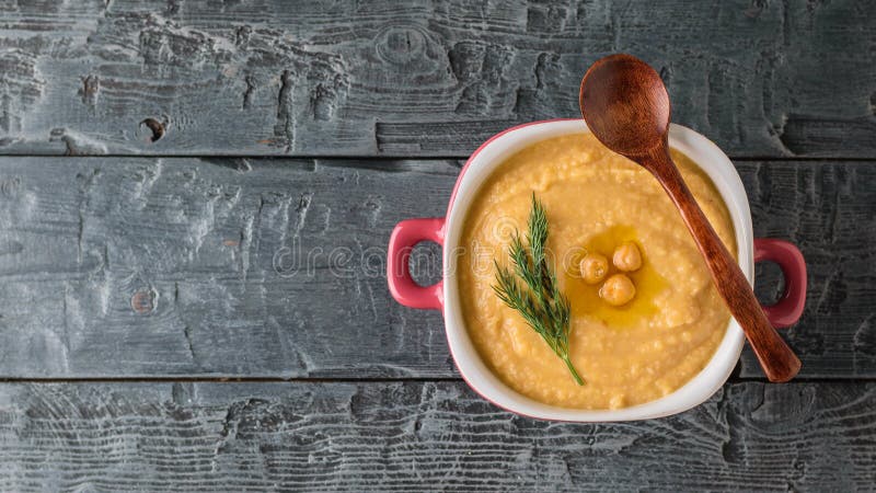 Hummus appena fatto in una ciotola porpora con un cucchiaio di legno su una tavola di legno scura La vista dalla parte superiore immagine stock libera da diritti
