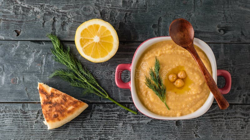 Hummus appena fatto in una ciotola porpora su una tavola con un pezzo di pane La vista dalla parte superiore fotografie stock libere da diritti