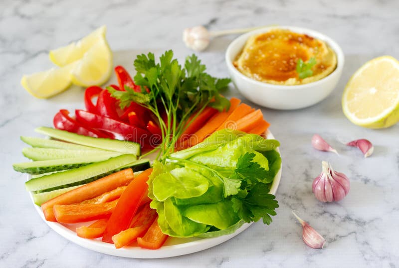 Hummus, different vegetables and lettuce leaves with lemon and garlic on a light background. Vegan food.