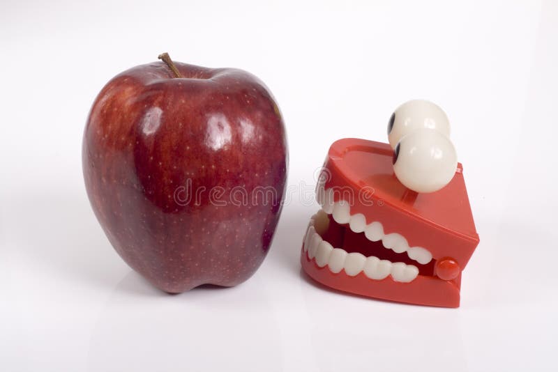 A red delicious apple with a pair of plastic toy false teeth with bug eyes staring at the apple..Concept of difficulty of eating certain foods when you have false teeth or dentures.Photographed against a white background. A red delicious apple with a pair of plastic toy false teeth with bug eyes staring at the apple..Concept of difficulty of eating certain foods when you have false teeth or dentures.Photographed against a white background.