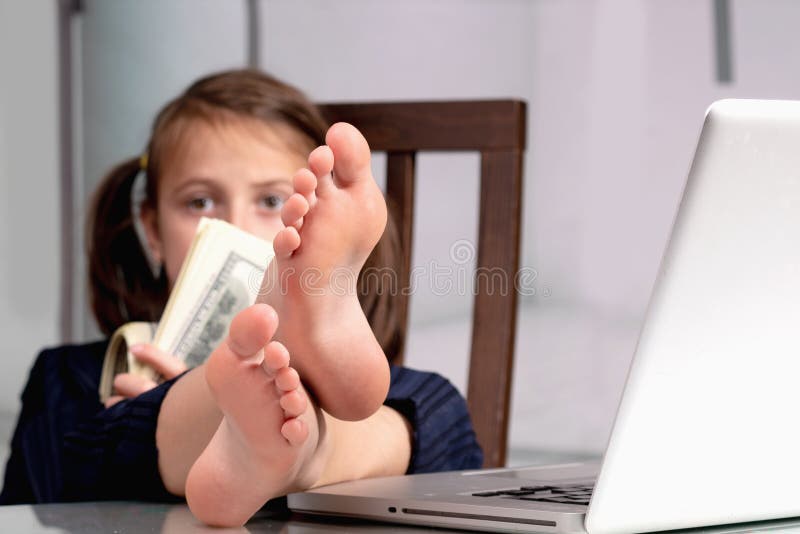 Humorous portrait of happy cute young business girl counts money profit with bare feet on the table. Selective focus on bare feet