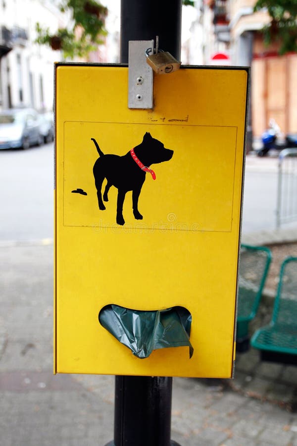 Yellow plastic bag dispenser for dog poo in park. Yellow plastic bag dispenser for dog poo in park