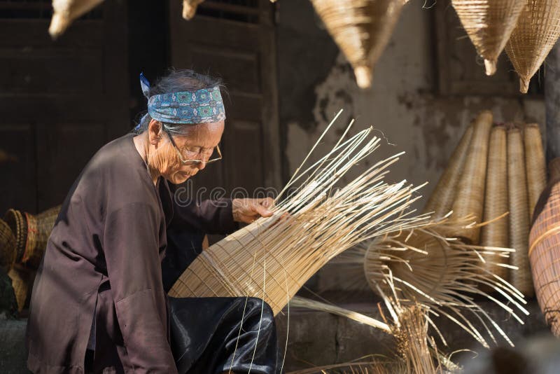 Hung Yen, Vietnam - 9. Juli 2016: Weiblicher Handwerker, der traditionelle Bambusfischfalle an ihrem alten Haus im Thu Sy-Handels stockbild Hung Yen, Vietnam - 9. Juli 2016: Weiblicher Handwerker, der traditionelle Bambusfischfalle an ihrem alten Haus im Thu Sy-Handels stockbild