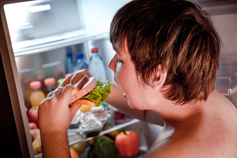 Hungrig man som rymmer en smörgås i hans händer och anseende bredvid arkivbild Hungrig man som rymmer en smörgås i hans händer och anseende bredvid arkivbild