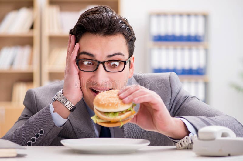 Hungriger witziger Geschäftsmann, der Sandwich der ungesunden Fertigkost essen