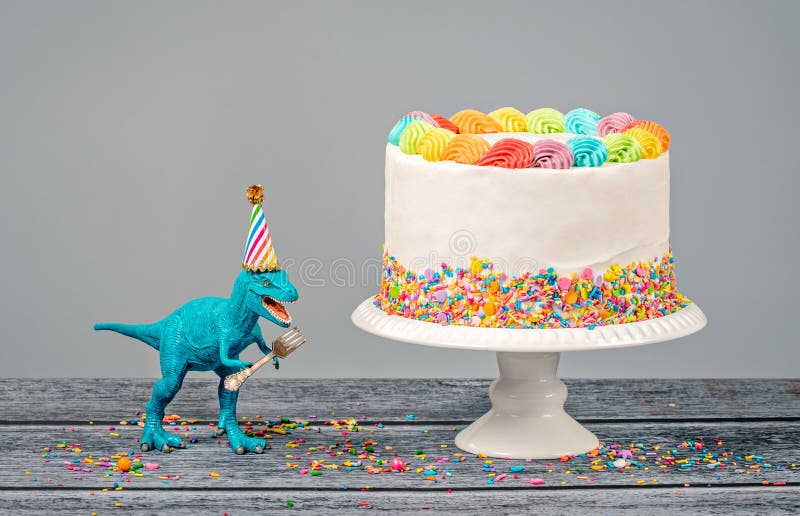 Hungry toy dinosaur wearing a hat and holding a fork next to a birthday Cak...