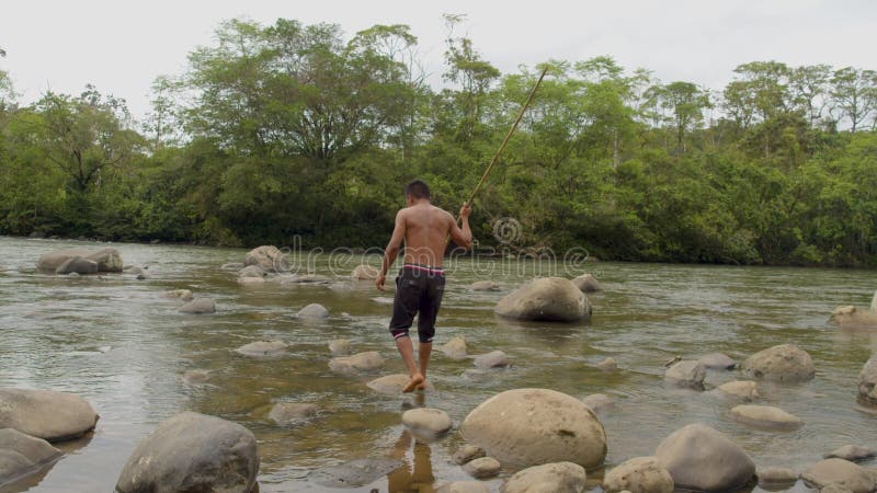 Hunter fishing with a spear by the river in the amazon rainforest