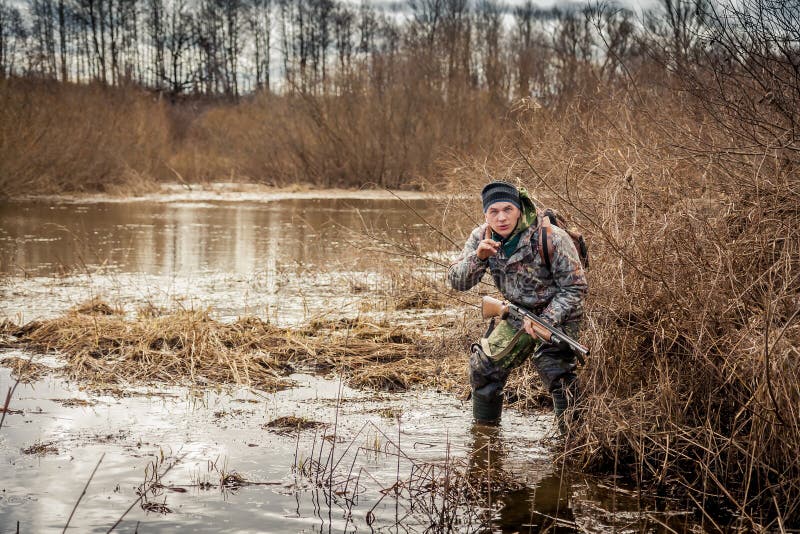 Hunter man wading through the swamp lurking in the bushes and shows gesture to be quiet stock image Hunter man wading through the swamp lurking in the bushes and shows gesture to be quiet stock image