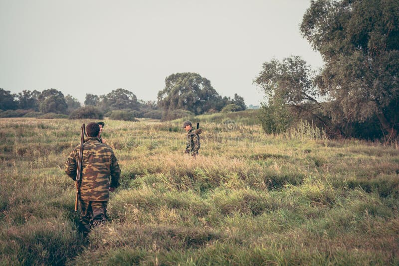 Hunters crossing through tall grass in rural field during hunting season