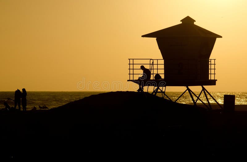 A silhouette of people and a lifeguard tower at sunset in Huntington Beach,CA during the summer.