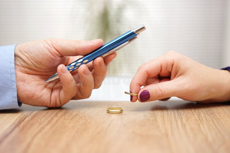 Husband is giving pen to sign divorce papers his former wife after he take off the ring form finger .