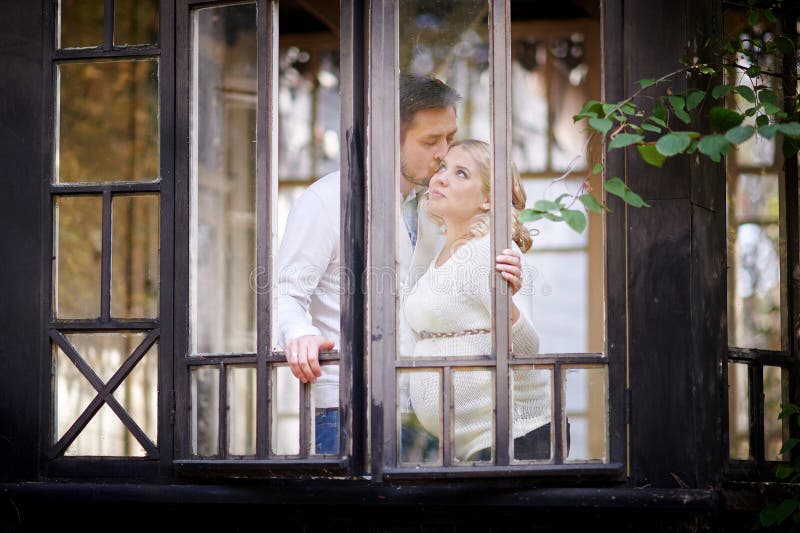 Husband kisses his pregnant wife in the house. View through window stock image Husband kisses his pregnant wife in the house. View through window stock image