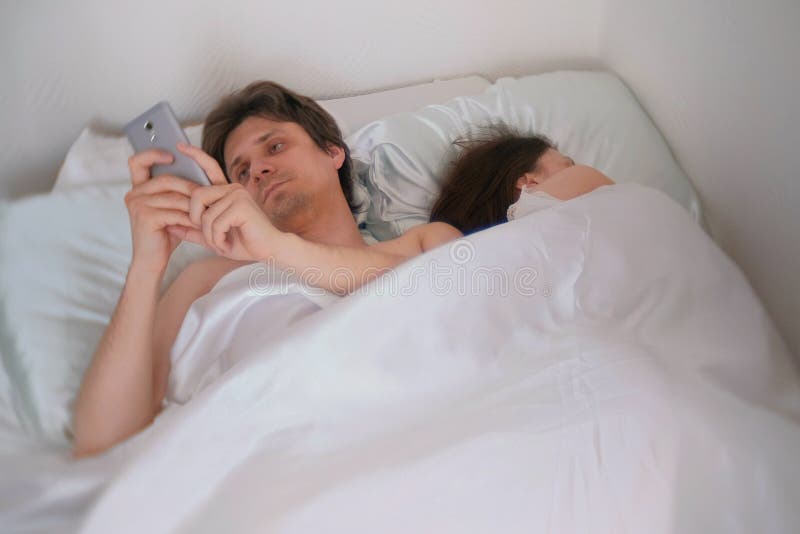 Husband is Watching Something in the Mobile Phone, while His Wife is Sleeping Away photo
