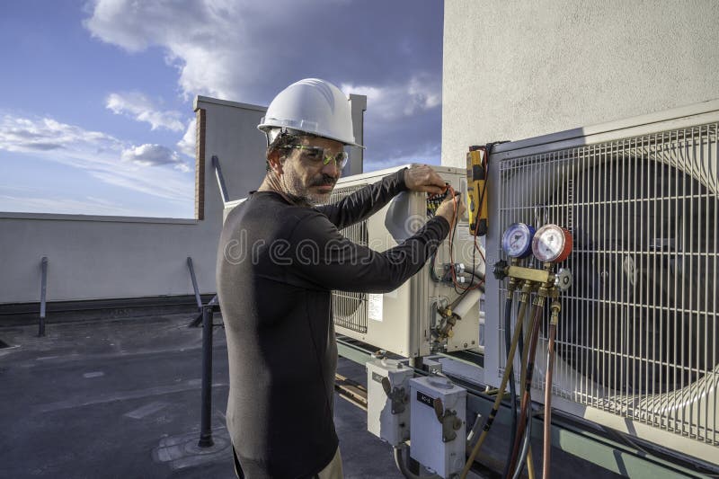 HVAC technician looking at camera, testing voltage on a mini split air conditioning system. HVAC technician looking at camera, testing voltage on a mini split air conditioning system
