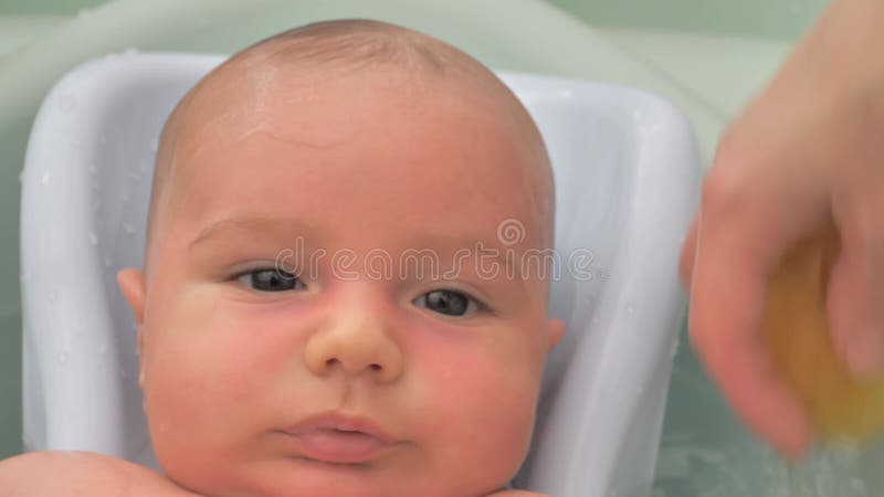 Hygienic procedures for newborns. Bathing a child in the bathroom. A happy baby in a bath. Warm water is poured over the